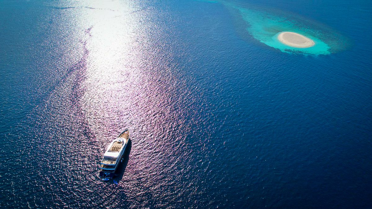 Scubaspa liveaboard anchored in deep blue water beside a reef edge in the Maldives, seen from the air