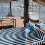 Sun deck daybeds with blue-striped cushions beneath the mast