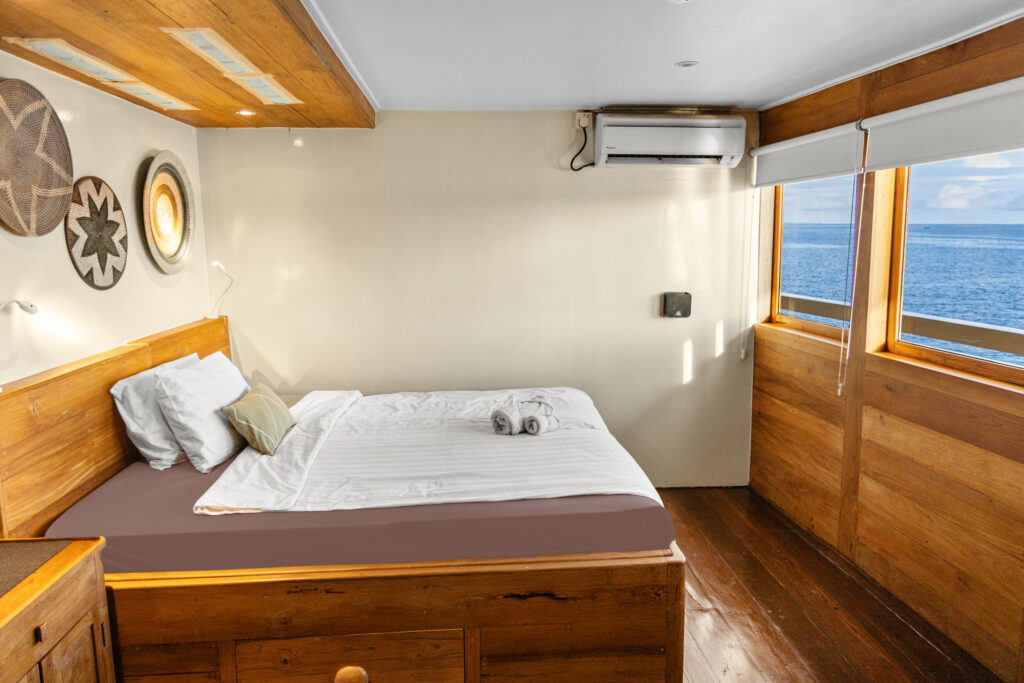 Cabin on the Emperor Harmoni liveaboard with a double bed, wooden panelling and sea-view windows