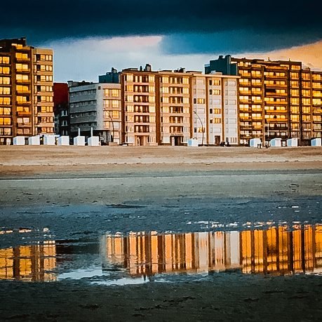 Apartment buildings along the De Panne Zeedijk reflected in the wet sand at dusk
