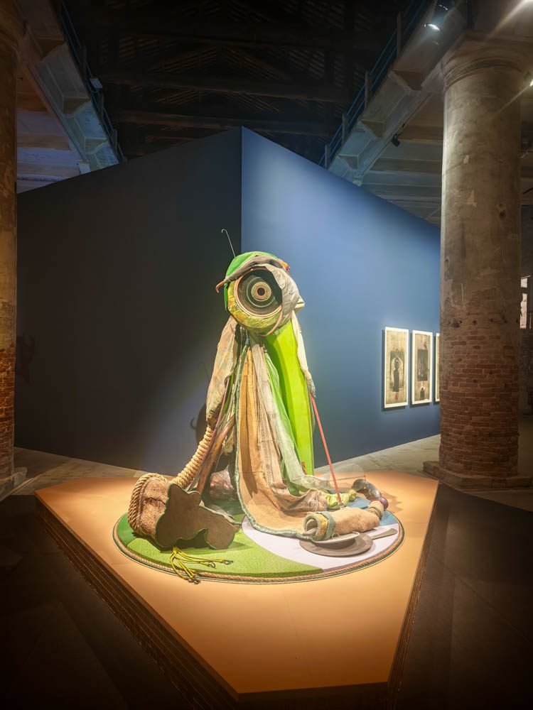 Textile sculpture lit on a plinth in a blue-walled Venice Biennale exhibition room