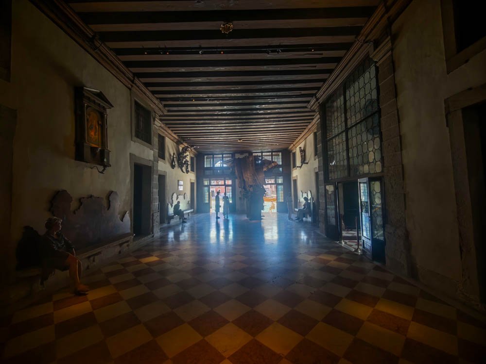 Long portego hall with a checkerboard marble floor inside a Venetian palazzo open for a Biennale collateral exhibition