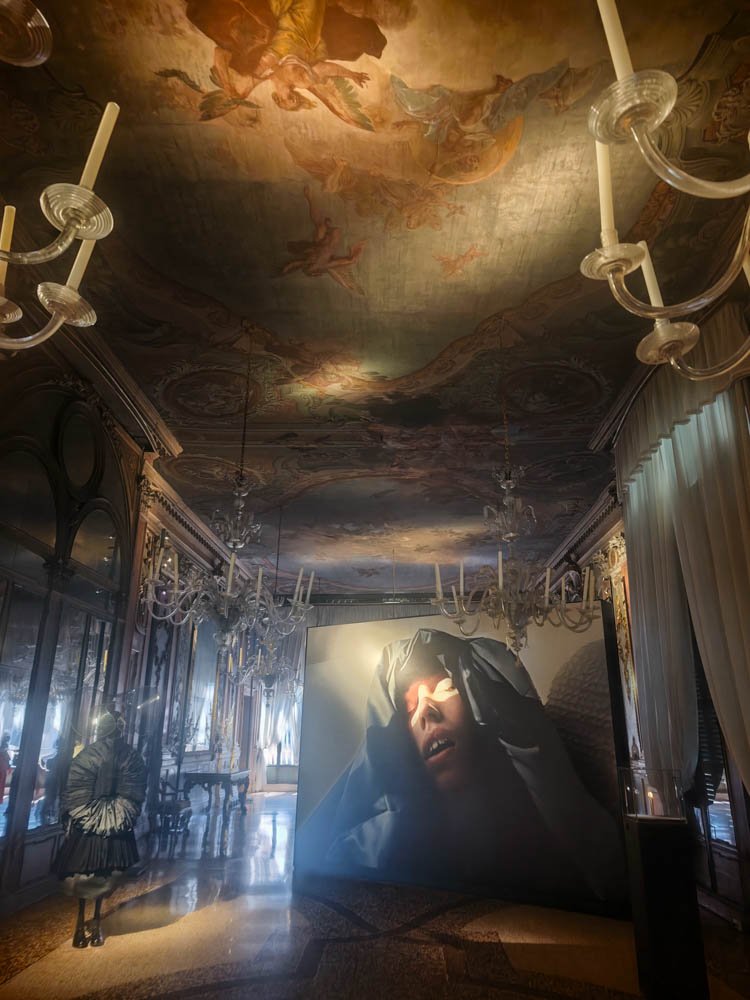 Frescoed palazzo hall with chandeliers hosting a free collateral exhibition during the Venice Biennale
