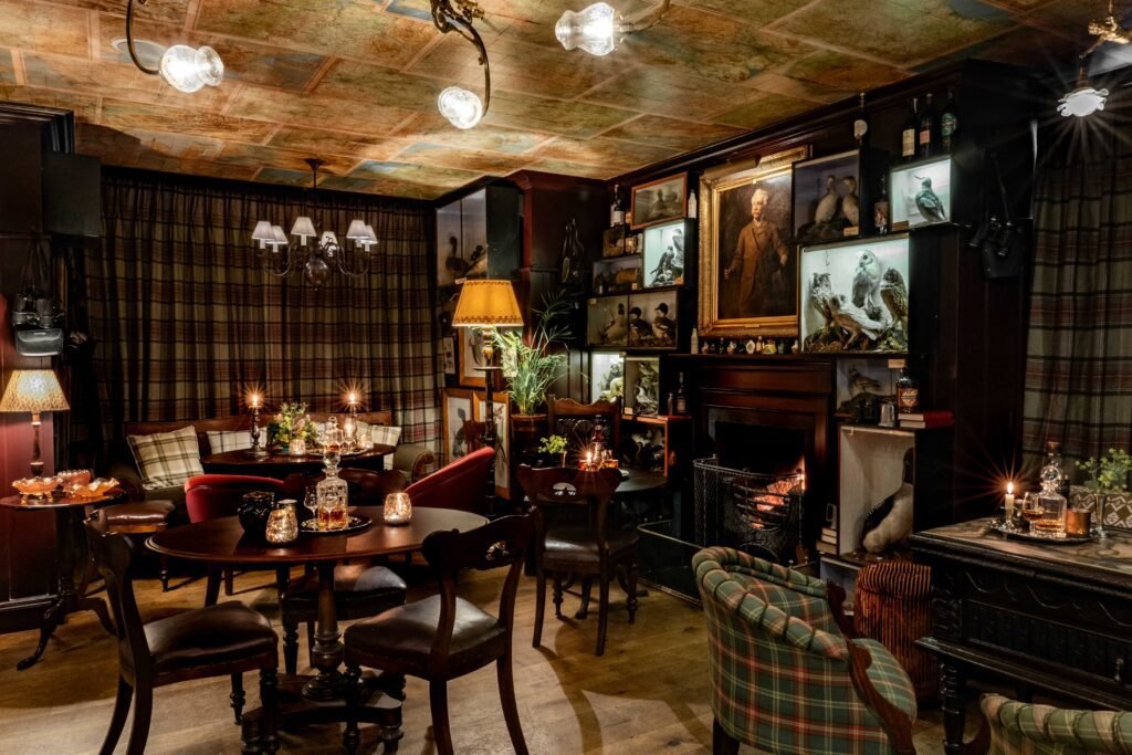 The candlelit bar at The Loch Lomond Arms, panelled in dark wood with Victorian taxidermy cases and a lit fire