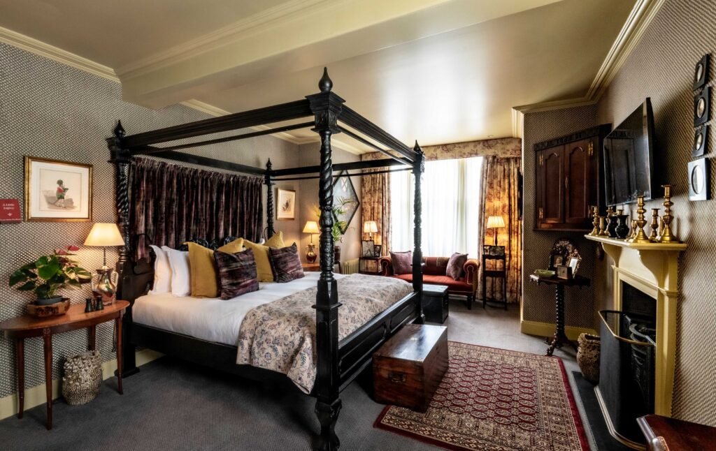 A bedroom at The Loch Lomond Arms with a carved black four-poster bed, velvet drapes and an open fireplace