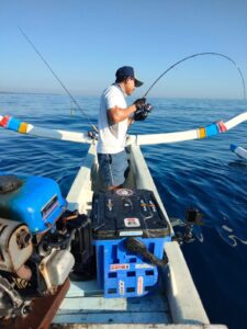 Fisherman reeling in a fish, rod bent, on a traditional jukung outrigger off Bukti, North Bali, fishing in Bali
