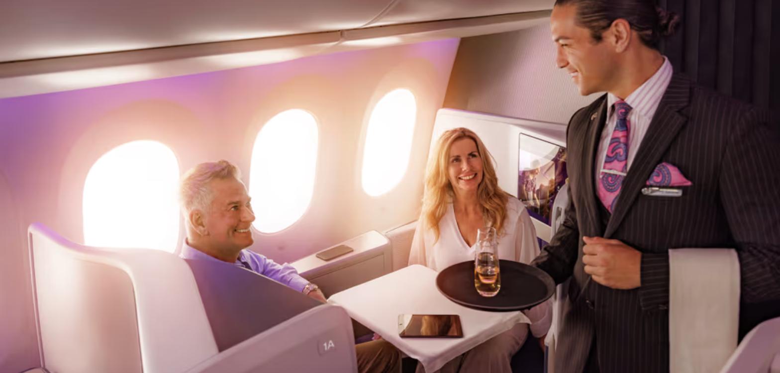 Two passengers dining in an Air New Zealand Business Premier Luxe seat as crew serve drinks