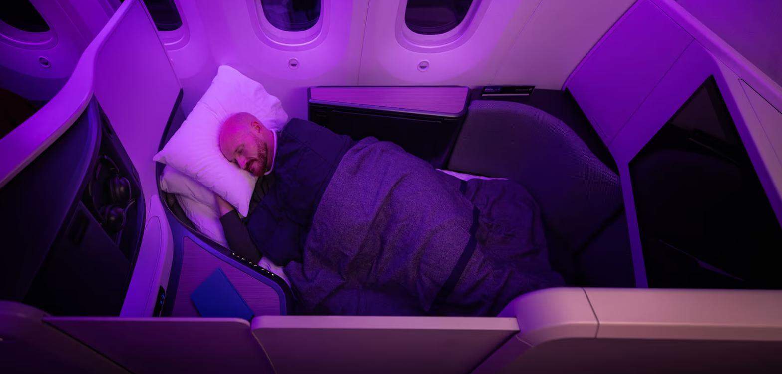 Passenger asleep under a duvet on the lie-flat bed in Air New Zealand Business Premier Luxe