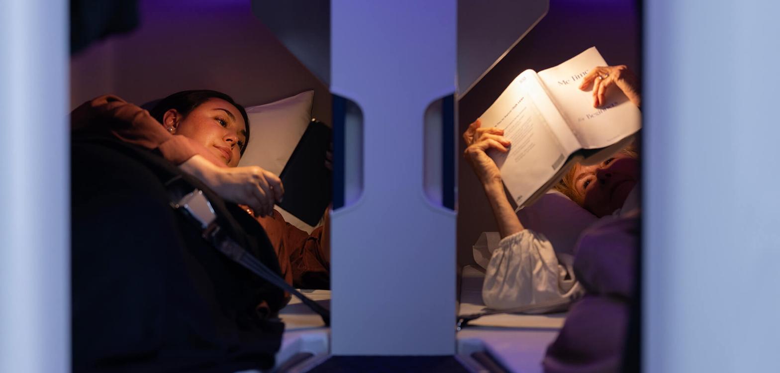Two passengers reading inside separate Air New Zealand Economy Skynest sleep pods