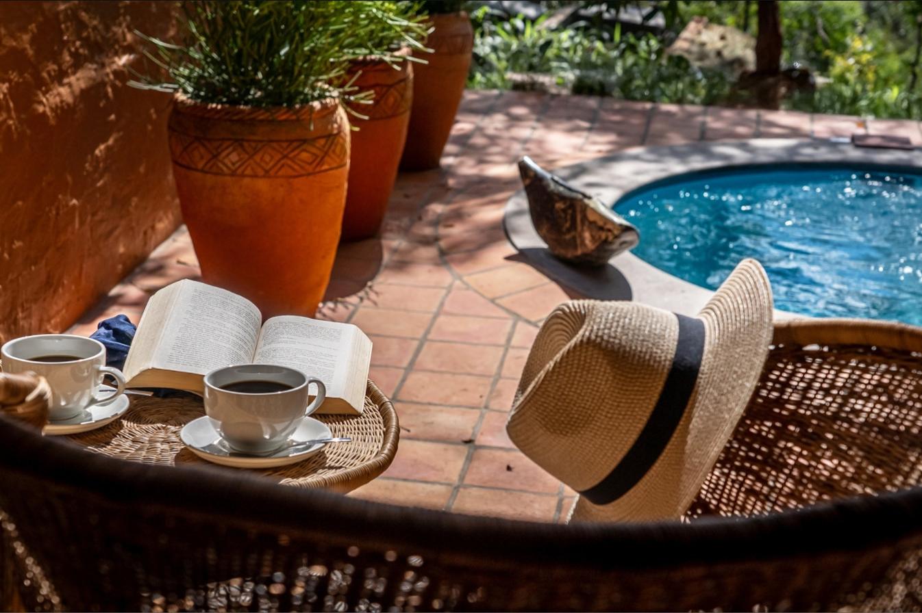 Coffee, a book and a sun hat on a wicker chair beside a villa plunge pool at Albida - Victoria Falls