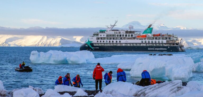 Yes, You Can Dive Antarctica — and This New Ship Is Built to Take You AE Expeditions’ Douglas Mawson lying off Cape Adare, Antarctica, with expeditioners in red parkas on the shore ice and a Zodiac running alongside