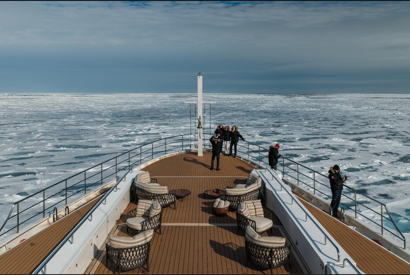 Guests on the teak foredeck lounge of Aqua Lares looking out over a horizon-wide field of broken Arctic sea ice