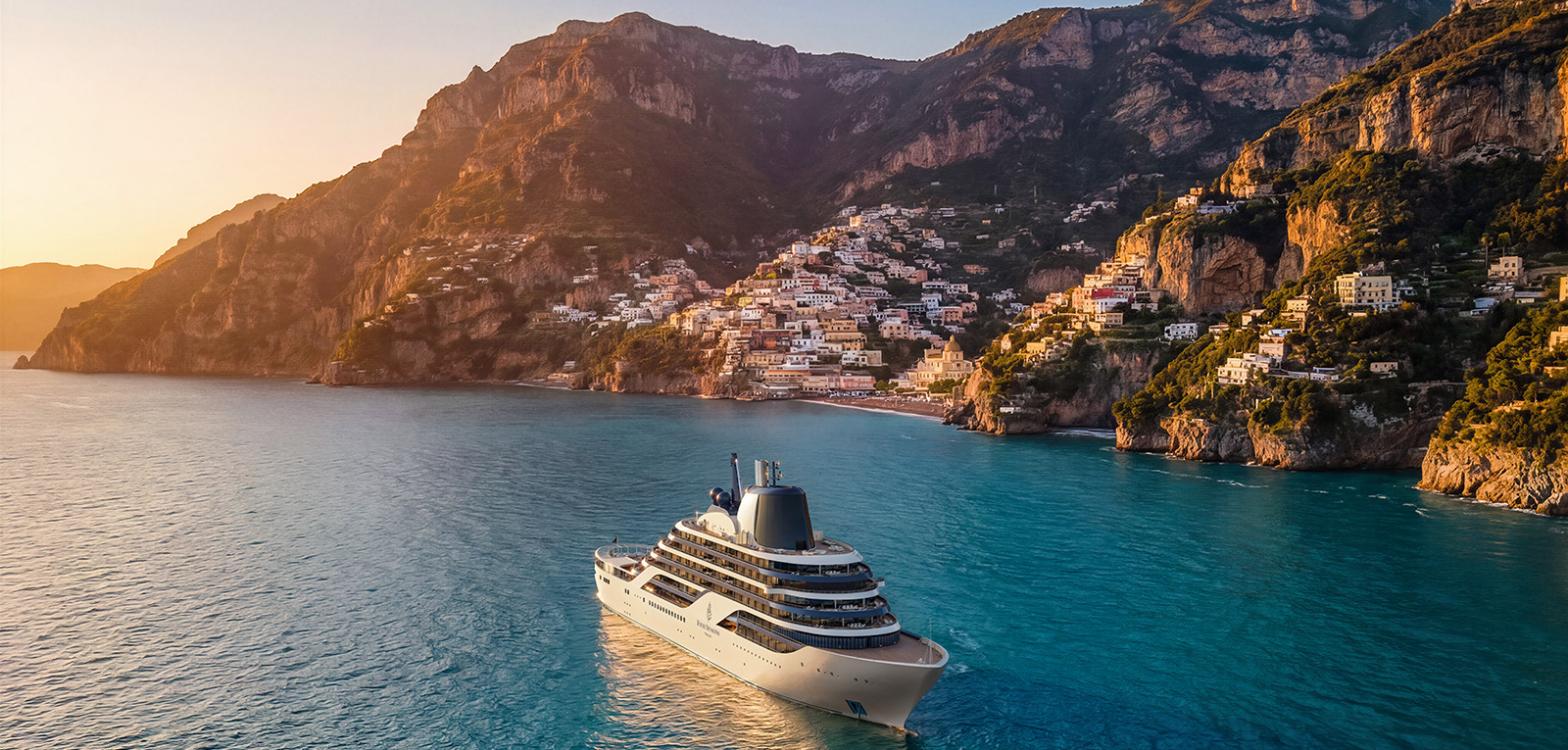 A rendering of the Four Seasons yacht at anchor in a turquoise bay below Positano at sunrise, its white hull and dark funnel set against the cliffside town