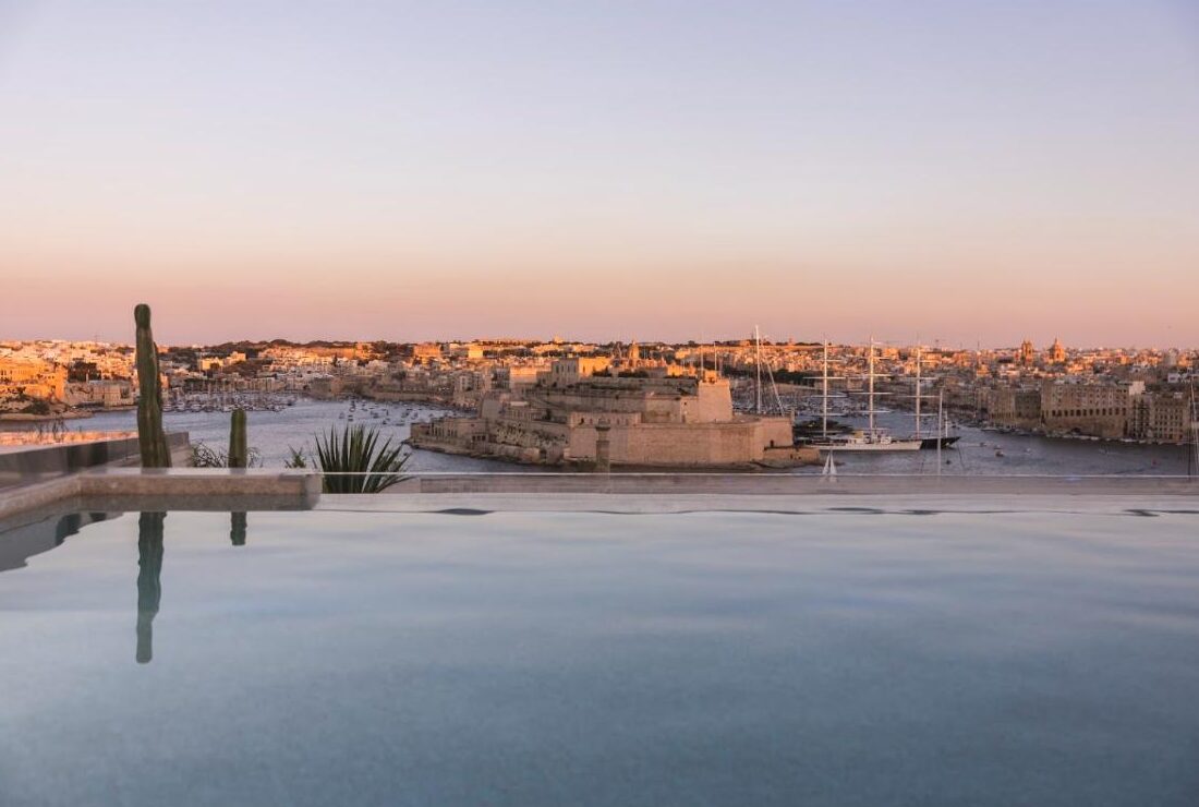 Rooftop pool above Iniala Valletta's Solis wing at sunset, looking across the Grand Harbour to the Three Cities