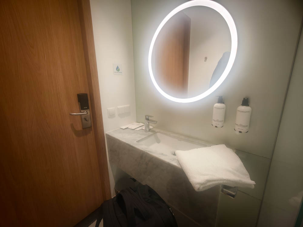 Sink with large illuminated round mirror in the KLM Crown Lounge 52 shower suite