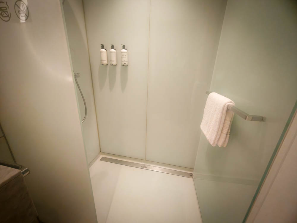 Shower cubicle with KLM-branded drain at Crown Lounge 52 — no bench and no bathmat