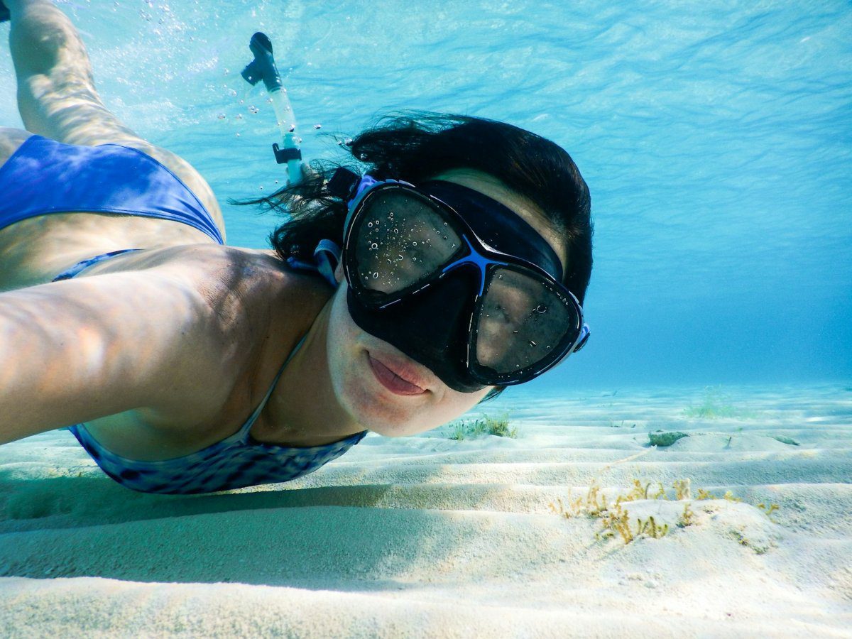 Snorkeller wearing a traditional two-lens low-volume mask swimming over sand in the Bahamas