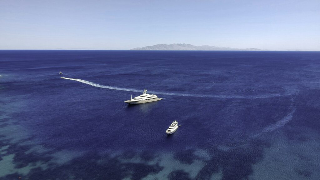 Two private yachts anchored in deep blue Aegean water off a Greek island
