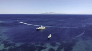 Two private yachts anchored in deep blue Aegean water off a Greek island