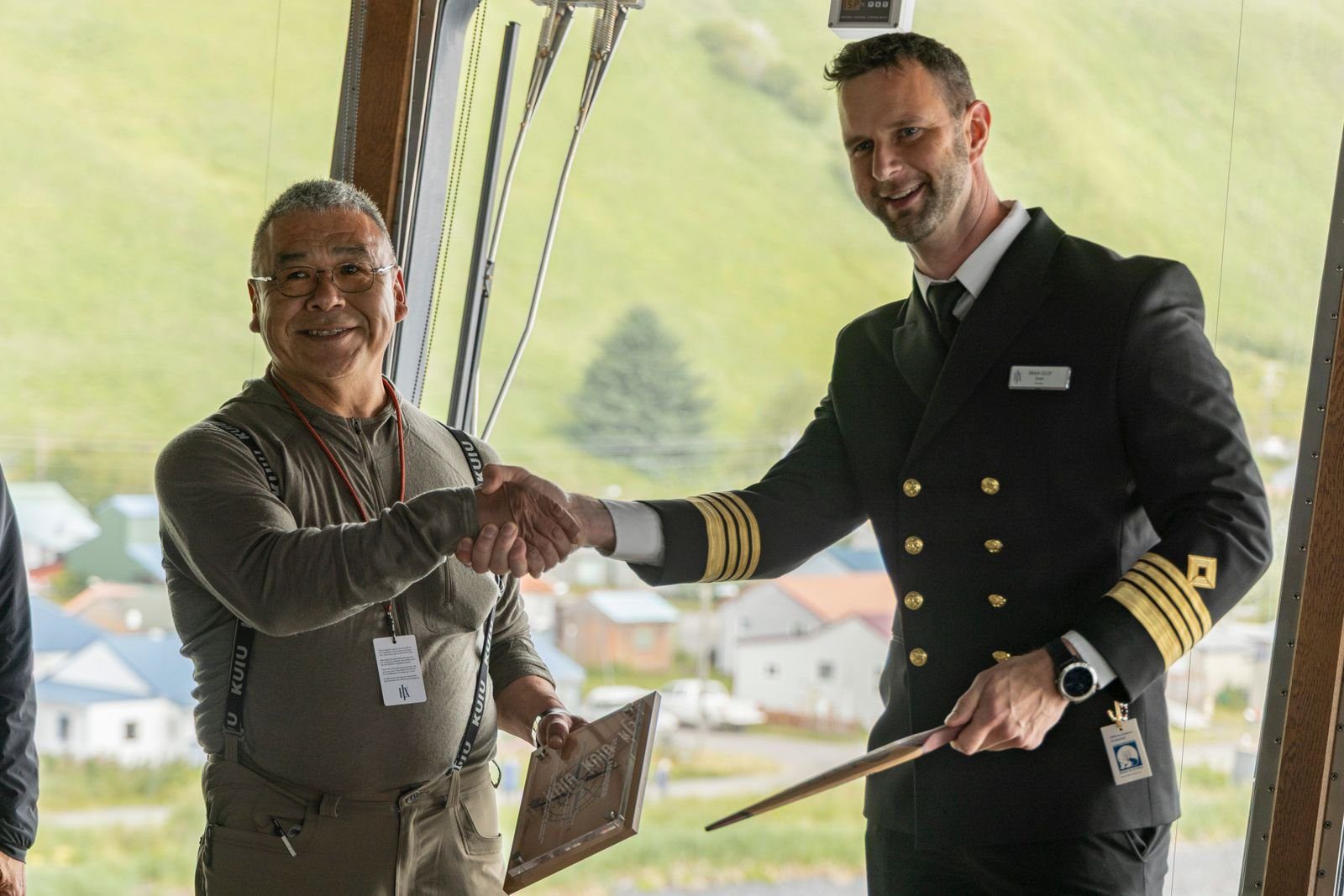 Chief Jeffrey Peterson of the Alutiiq Tribe of Old Harbor shakes hands with Captain Bram Olof of MS Roald Amundsen while presenting him with a ceremonial paddle