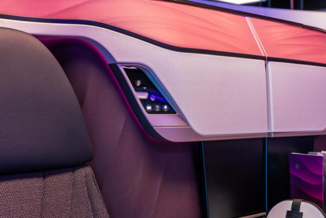 Qsuite Next Gen suite shell and seat under coral mood lighting, with the in-suite service panel