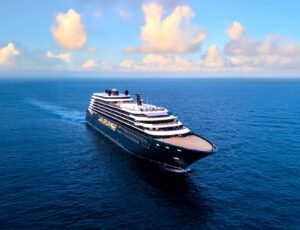 Luminara under way on open blue water, seen from the air off her port bow, with tiered white decks above a dark hull