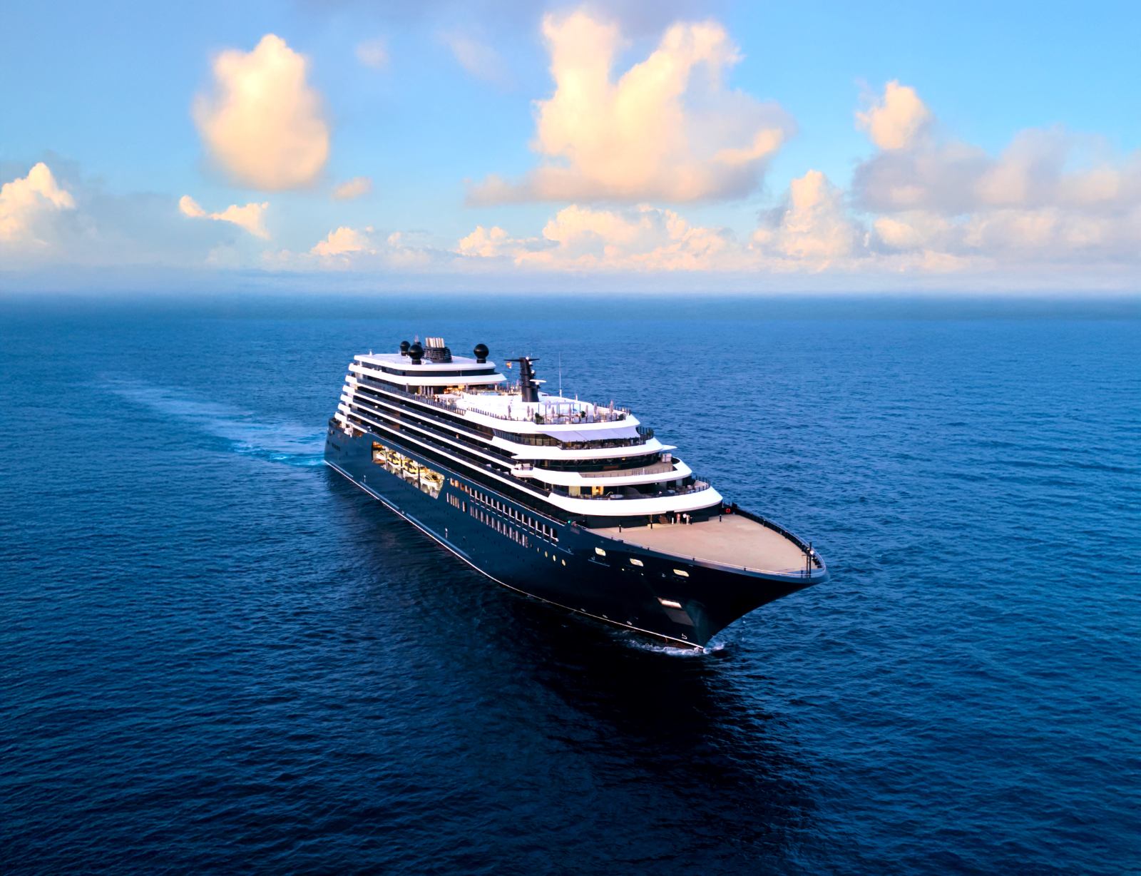 Luminara under way on open blue water, seen from the air off her port bow, with tiered white decks above a dark hull