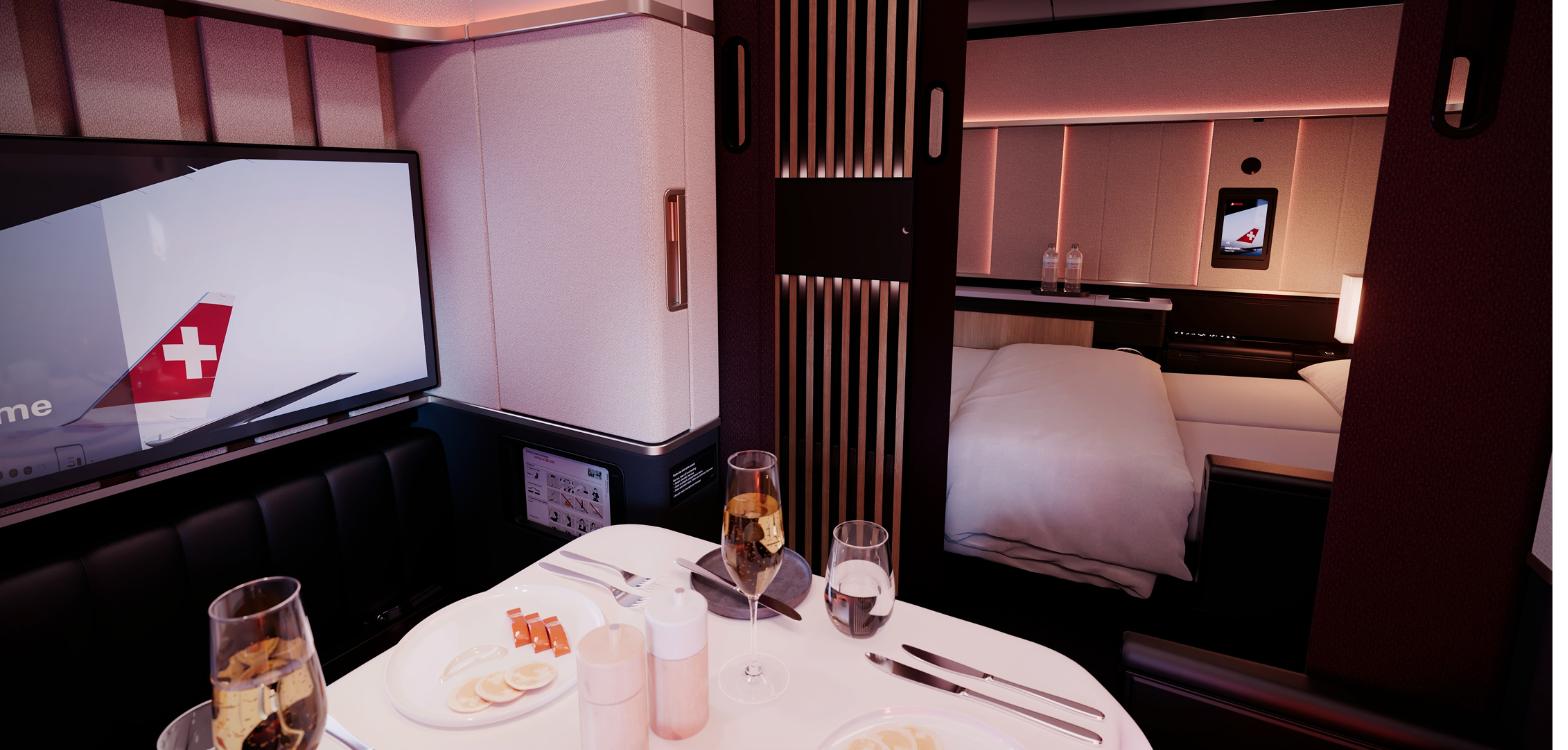 Dining table laid for a meal in a SWISS Senses First suite with the bed made up behind