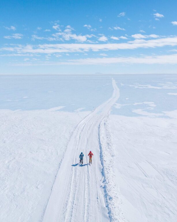 Aerial view of two people walking along a groomed track across the Antarctic ice sheet at a White Desert camp, part of the Lindblad White Desert deal