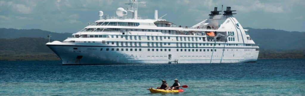 Two guests kayaking beside a Windstar Star Class yacht at anchor, the kind of water access offered from the Marina platform
