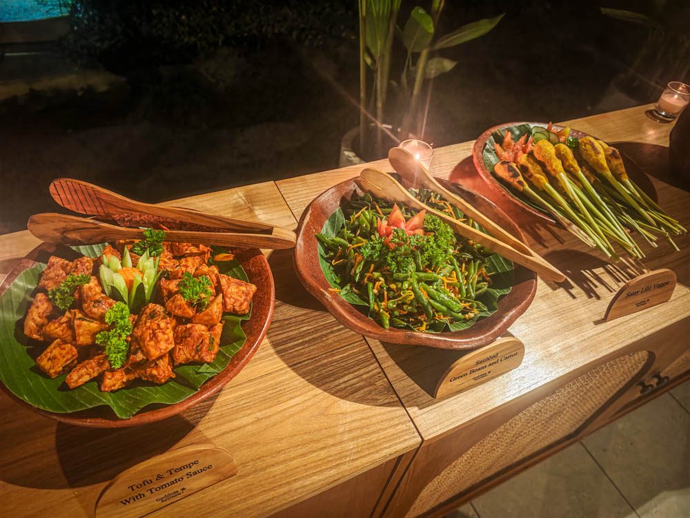 Themed dinner buffet in carved wooden bowls on banana leaves with labelled dishes and sate lilit at Goddess Retreat Ubud