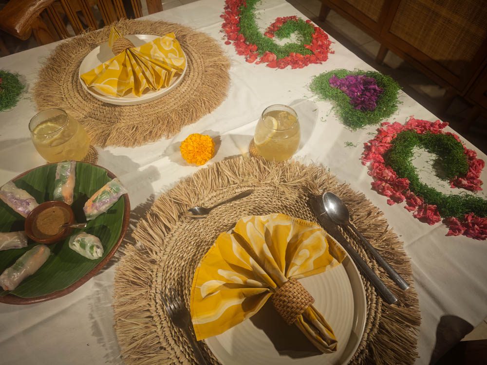 Dinner table with flower-petal designs, yellow napkins on rattan placemats and fresh spring rolls at Goddess Retreat Ubud