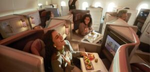 Passengers in Air India Business Class suites enjoying plated appetizers and drinks at linen-set tables, with crew serving in the aisle