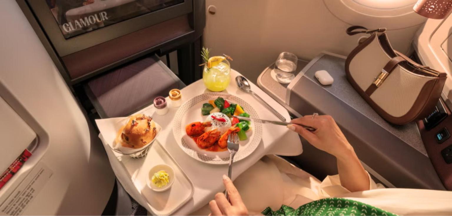 A plated prawn main course with rice and vegetables, bread, a Martaban-style salt and pepper set and a cocktail: Air India Business Class fine dining on a linen-covered table