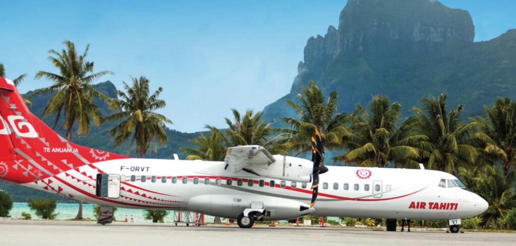 An Air Tahiti ATR 72 in red and white livery on the tarmac at Bora Bora airport, with palms, the lagoon and Mount Otemanu behind