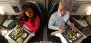 Two passengers eating salads at their seats in Alaska Airlines Boeing 787 Suites, with amenity kits and menus on the side consoles