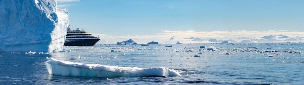 An Atlas Ocean Voyages ship dwarfed by icebergs and glaciers in Antarctica, from the line's 2028/29 Antarctica season campaign