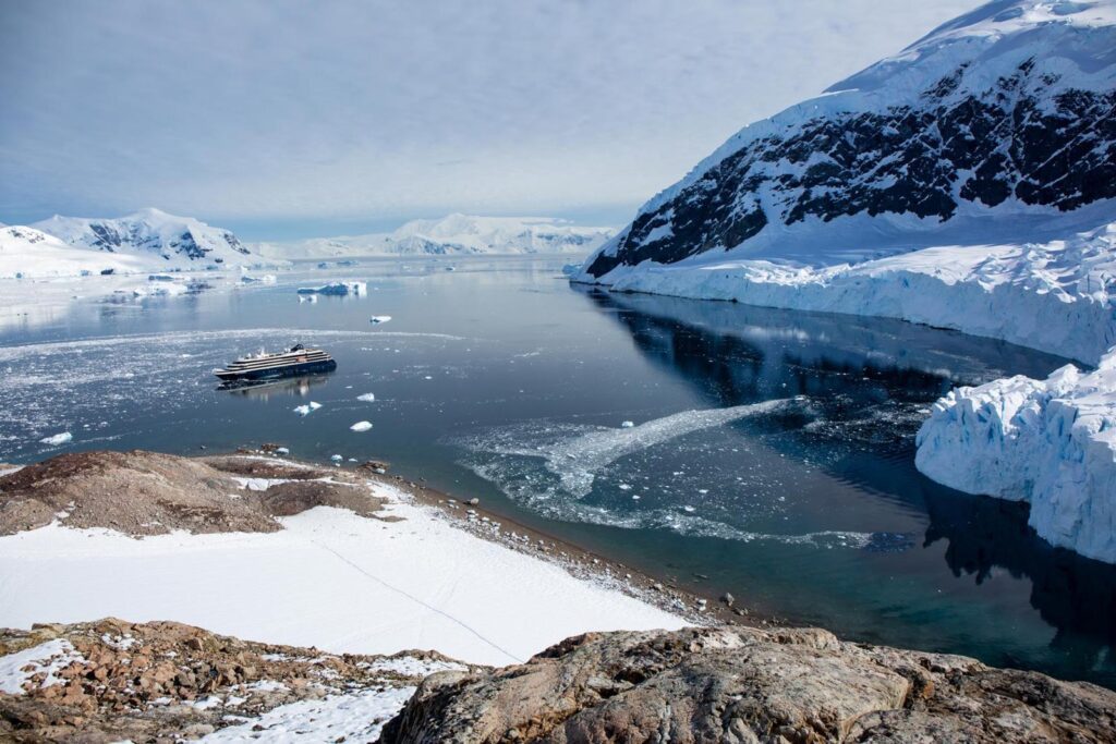 Atlas Ocean Voyages World Navigator at anchor in an Antarctic bay, with Zodiacs heading for a rocky shore