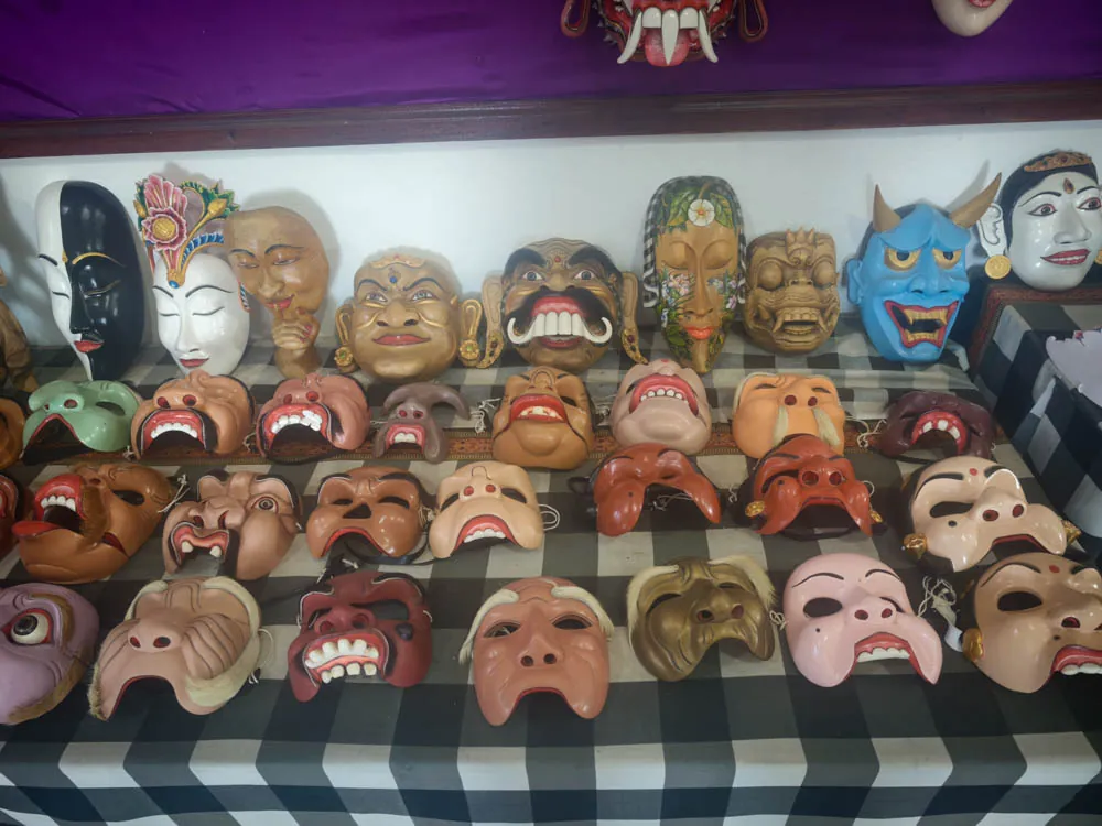 Rows of painted Balinese masks on a black-and-white poleng cloth in a mask maker's studio in Mas