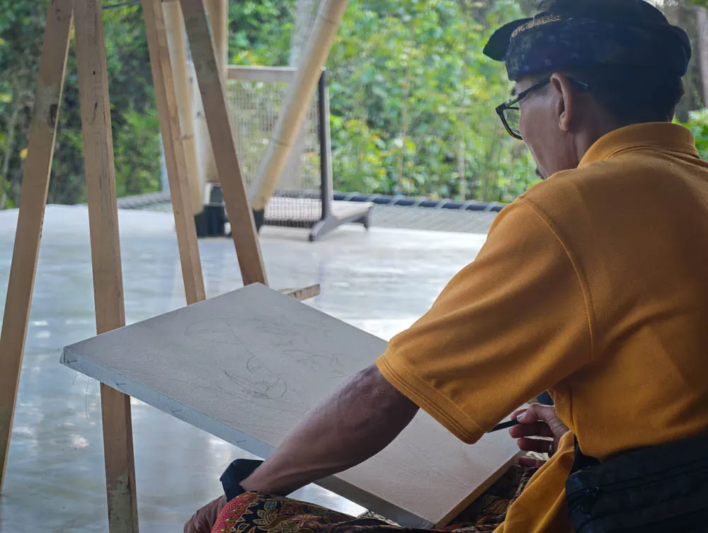 Balinese master painter sketching an outline on canvas at an easel in the yoga shala