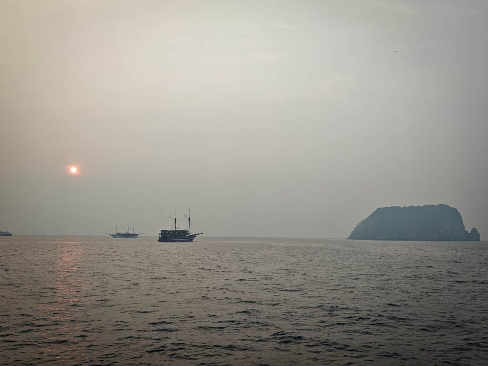 Sun dimmed by forest-fire haze over the Banda Sea, with a liveaboard on the horizon
