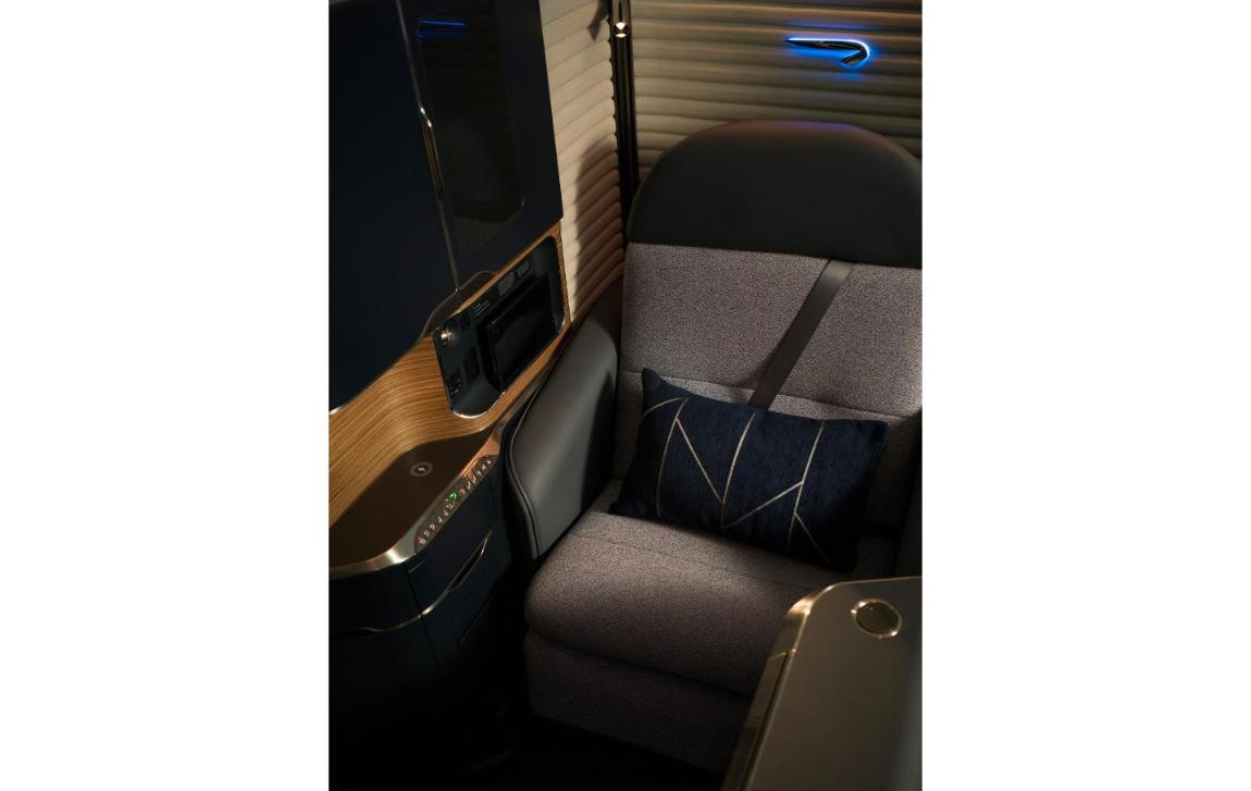 The new British Airways A380 First suite with grey upholstered seat, navy day cushion, wood-effect console and a lit Speedmarque on the suite wall