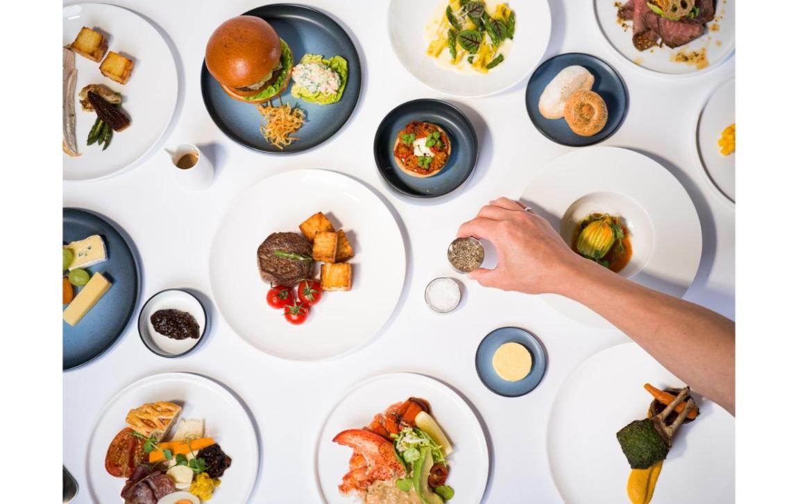 Overhead view of British Airways new First Class dishes on white and blue plates, including steak with potatoes, a burger, lobster and a rack of lamb