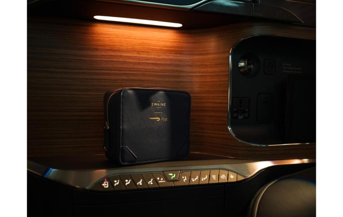 The navy Swaine amenity kit for British Airways First on a wood-panelled suite console next to the seat controls