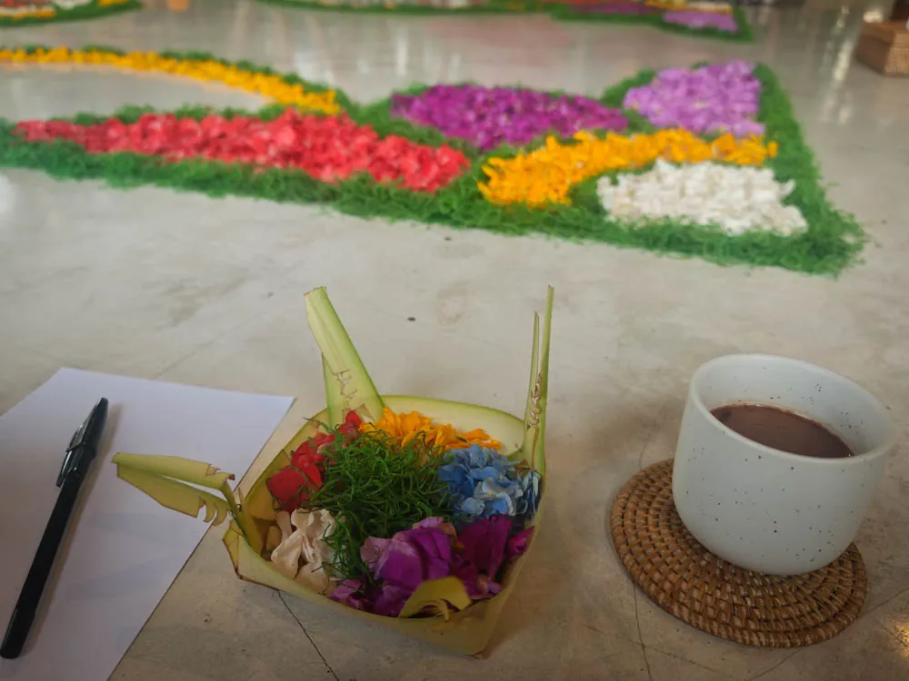 Canang sari offering of palm leaf and flowers made at the workshop, next to a cup of ceremonial cacao
