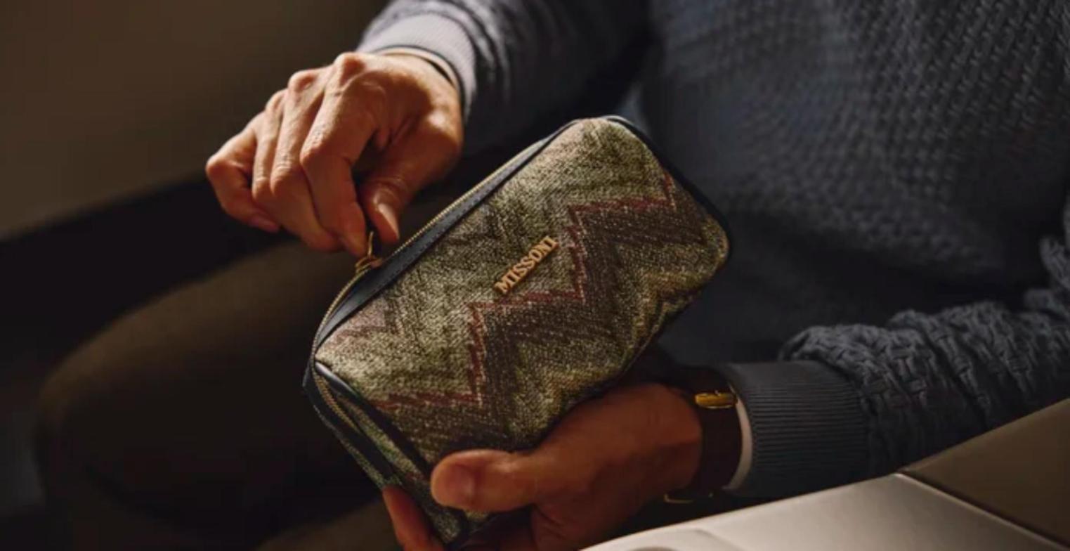 A passenger unzips the new Missoni Winter Elsewhere amenity kit in zig-zag woven fabric in a Delta One suite