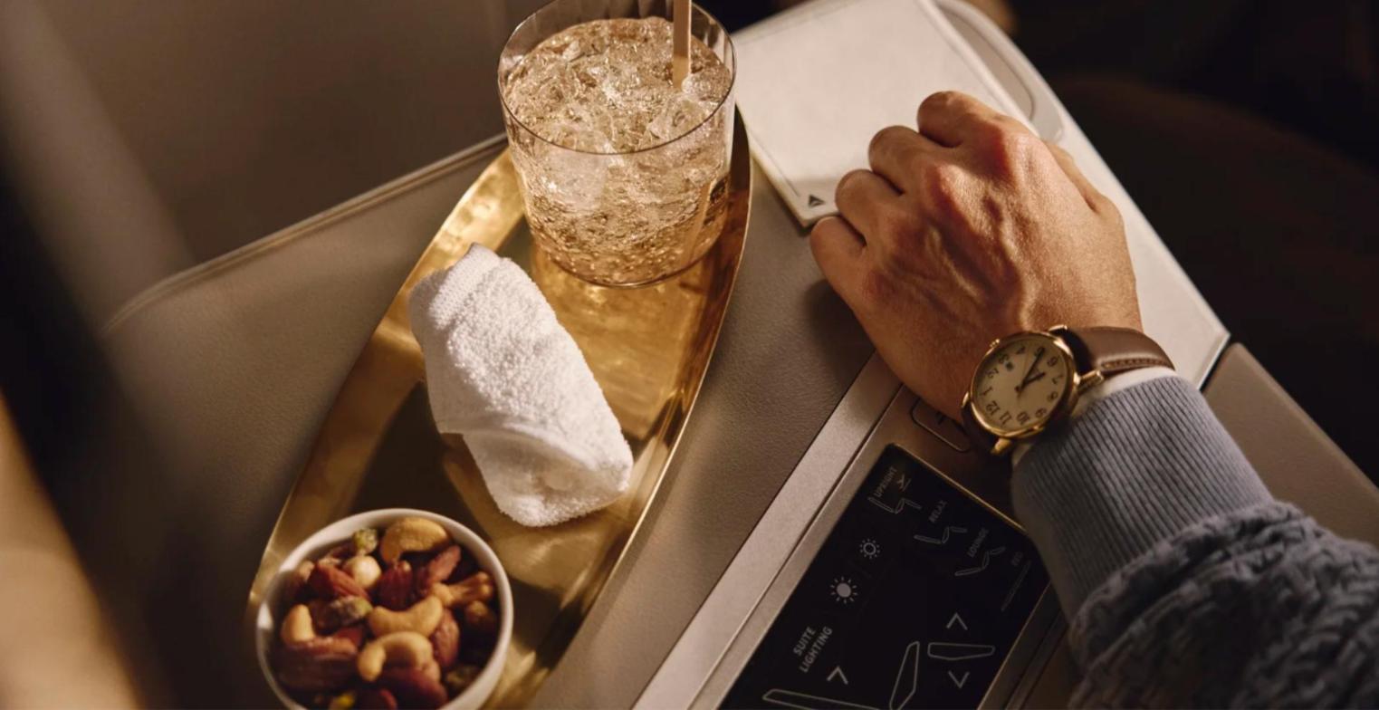Delta One Sip and Settle service: a welcome drink, hot towel and warm nuts on a brass tray beside the suite controls