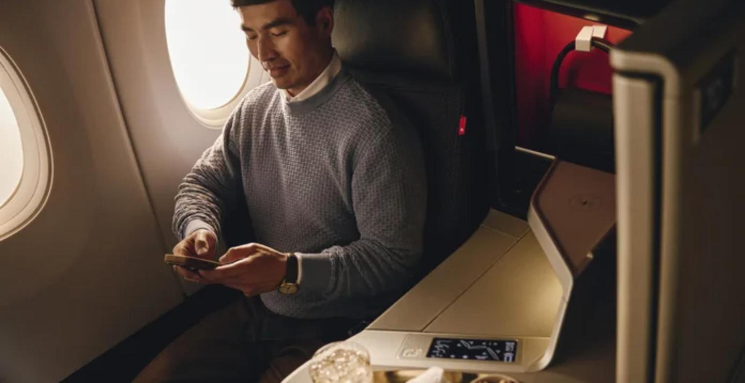 A passenger in a Delta One suite checks his phone beside the console as the new Delta One service's Sip and Settle drink and nuts are served