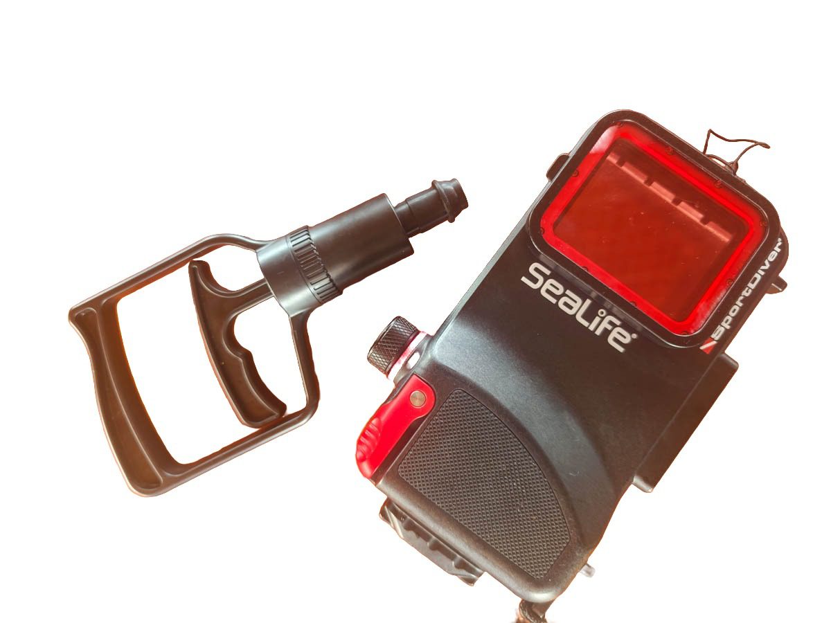 SeaLife SportDiver Ultra black polycarbonate underwater phone housing with its red front window, next to the hand-operated vacuum pump used for the pre-dive seal check