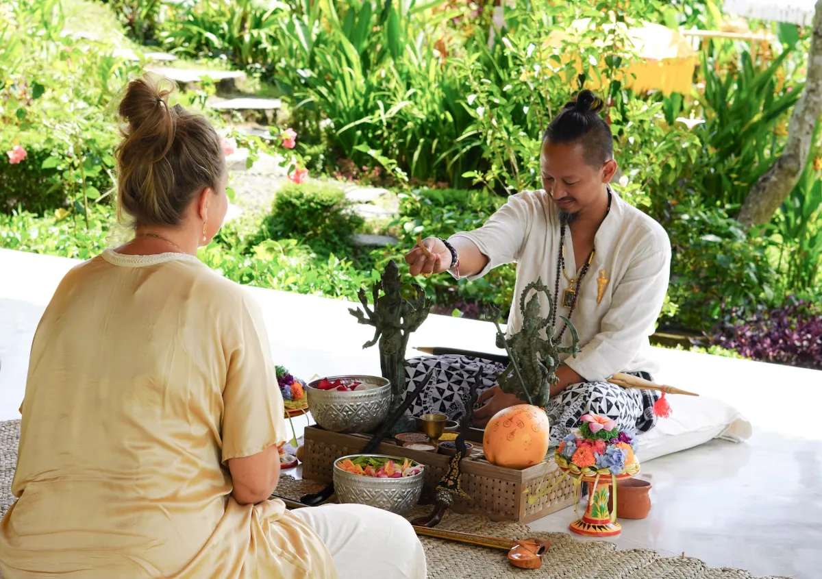 Balinese healer preparing an offering for a guest in a tropical garden in Bali